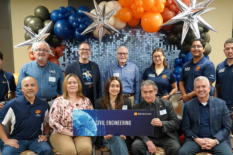 Two attendees pose together at a banquet table during a UTEP Engineering homecoming gathering, seated among event decorations, table centerpieces, and other guests in a banquet-style event space.